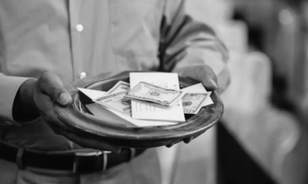 Hands holding an offering plate containing money and envelopes