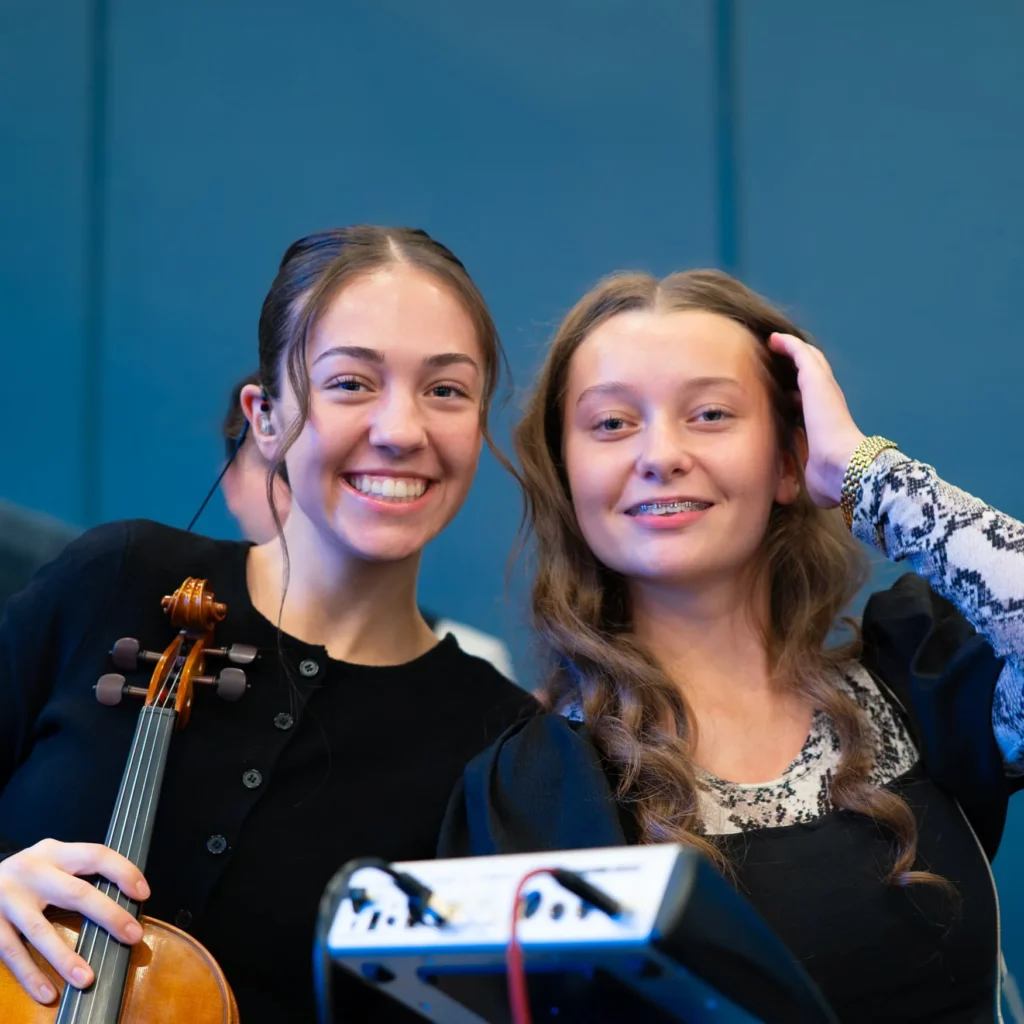 Two smiling young people at church, one holding a violin