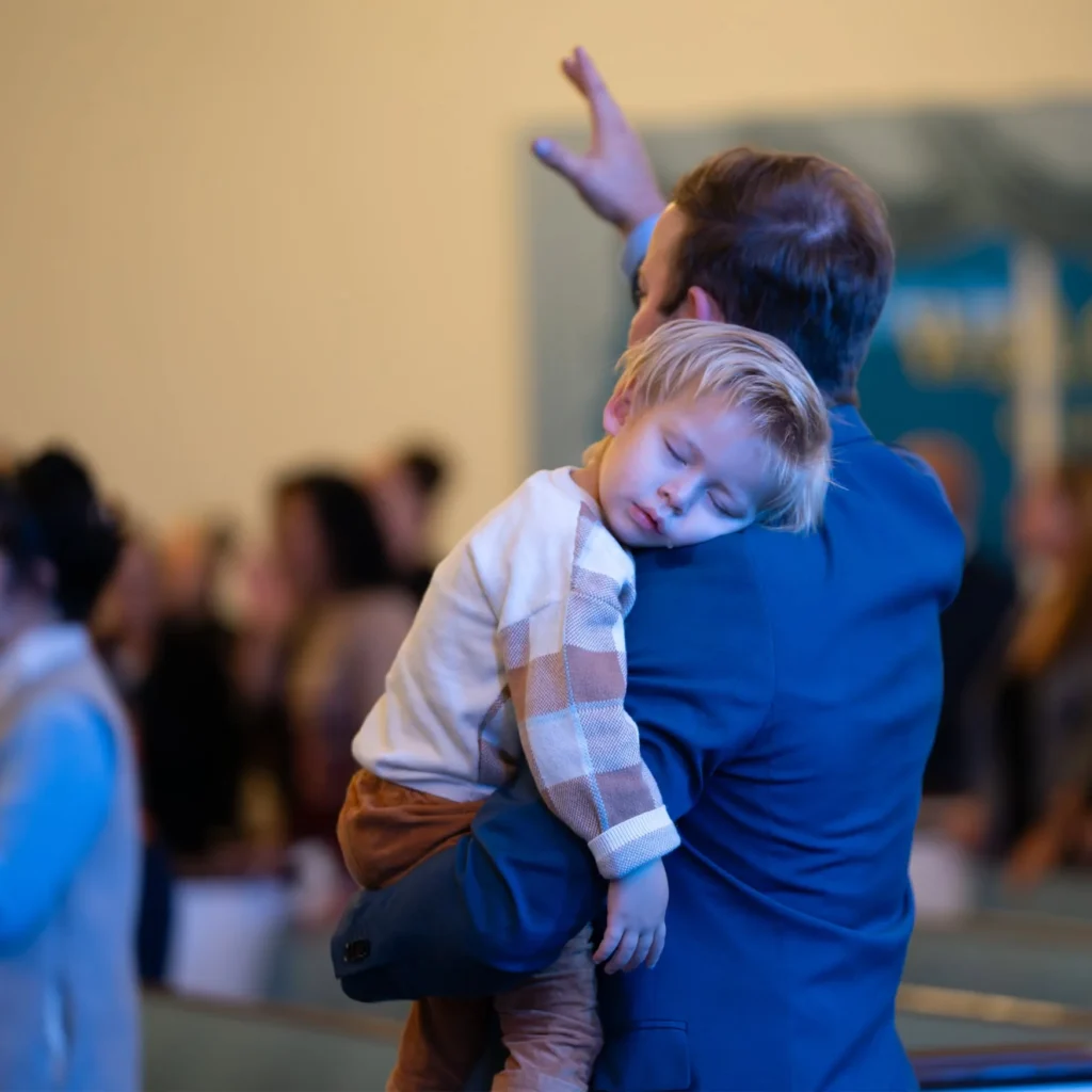 Adult holding a sleeping young child with one hand raised during worship